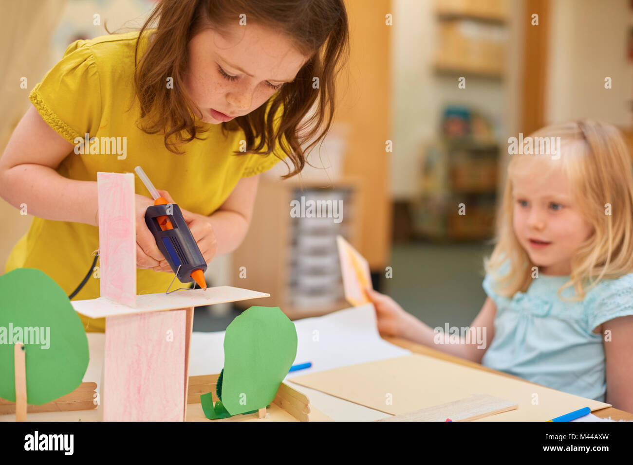 Primary schoolgirls making cardboard model at classroom desk Stock Photo