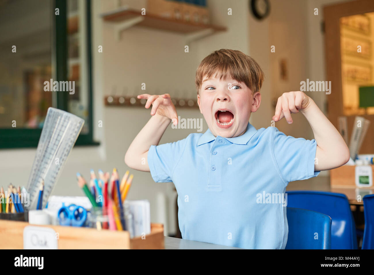 Primary schoolboy mimicking monster in classroom Stock Photo