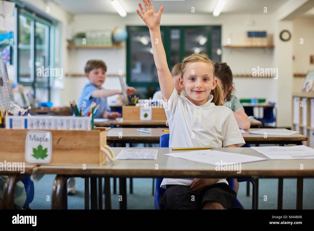 Schoolgirl with hand raised in classroom at primary school Stock Photo