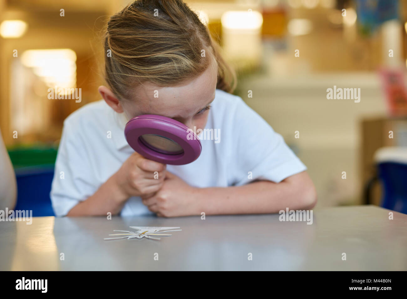 Schoolgirl looking through magnifying glass in classroom lesson at primary school Stock Photo