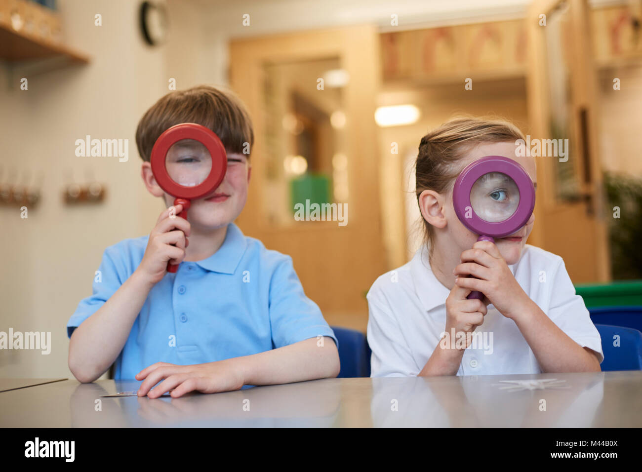 Schoolboy and girl looking through magnifying glasses in classroom at primary school, portrait Stock Photo