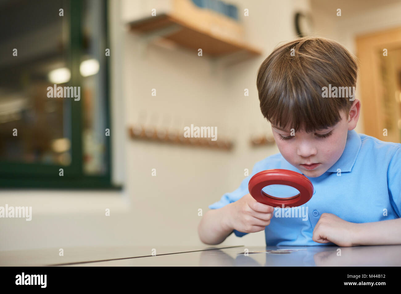 Schoolboy looking through magnifying glass in classroom lesson at primary school Stock Photo