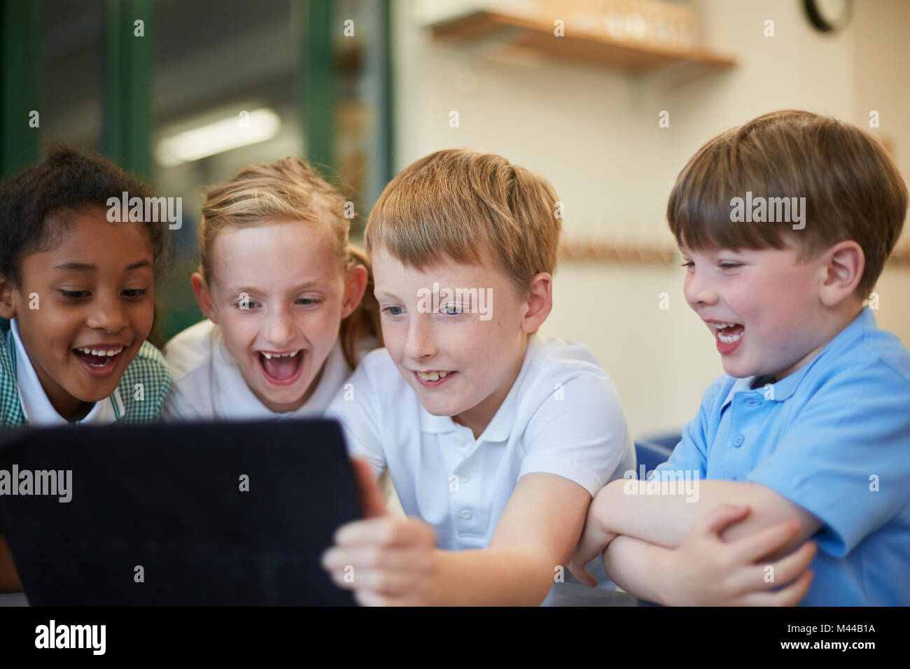 Schoolboys and girls laughing at digital tablet in classroom at primary school Stock Photo