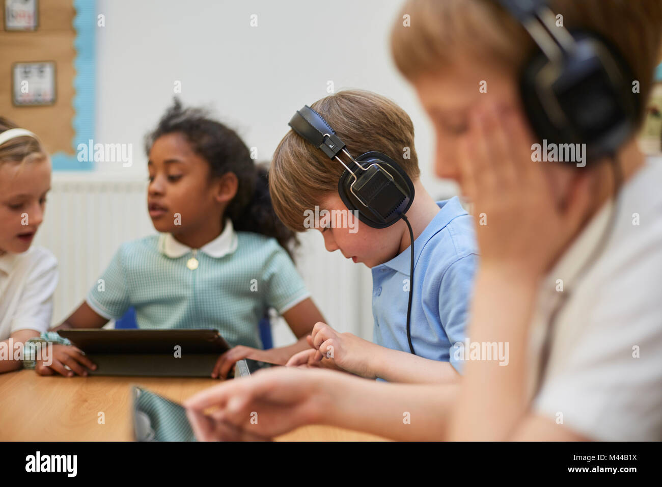 Schoolboys and girl listening to headphones in class at primary school Stock Photo