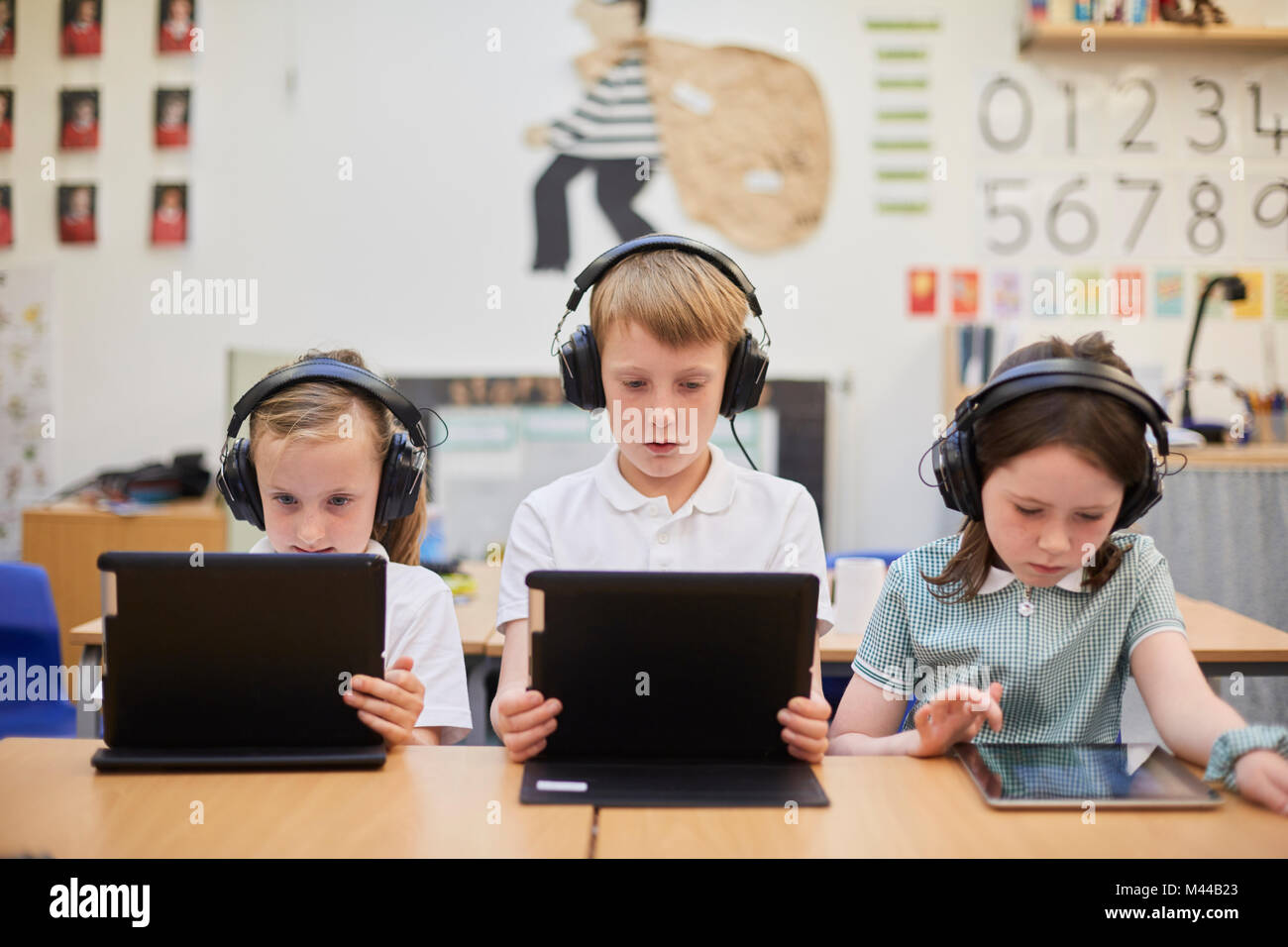 Schoolboy and girls listening to headphones in class at primary school Stock Photo