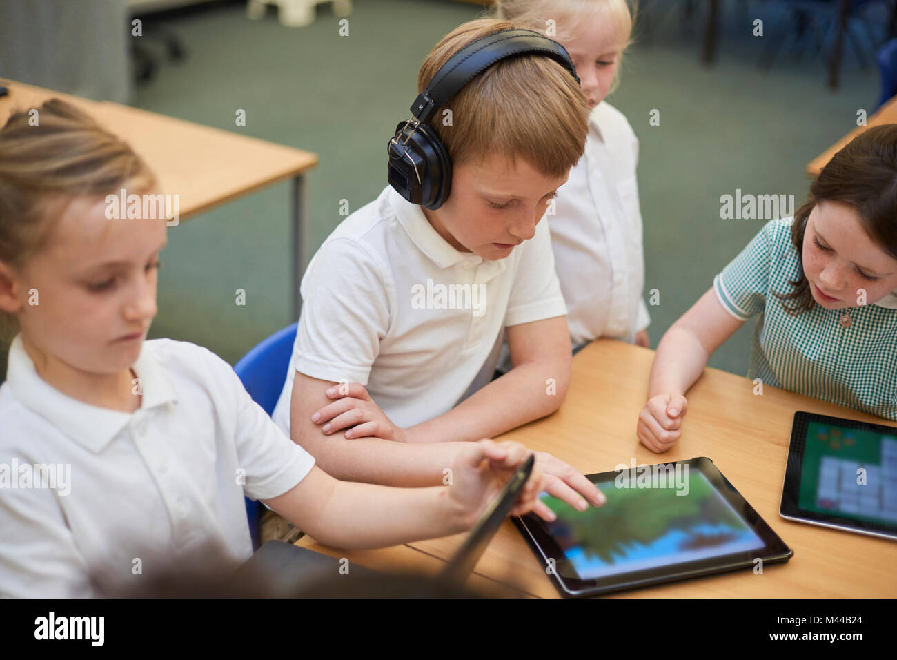 Schoolboys and girls looking at digital tablets in class at primary school Stock Photo