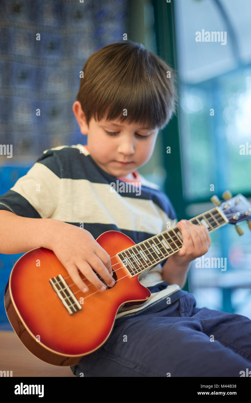 Schoolboy playing ukulele  in classroom at primary school Stock Photo