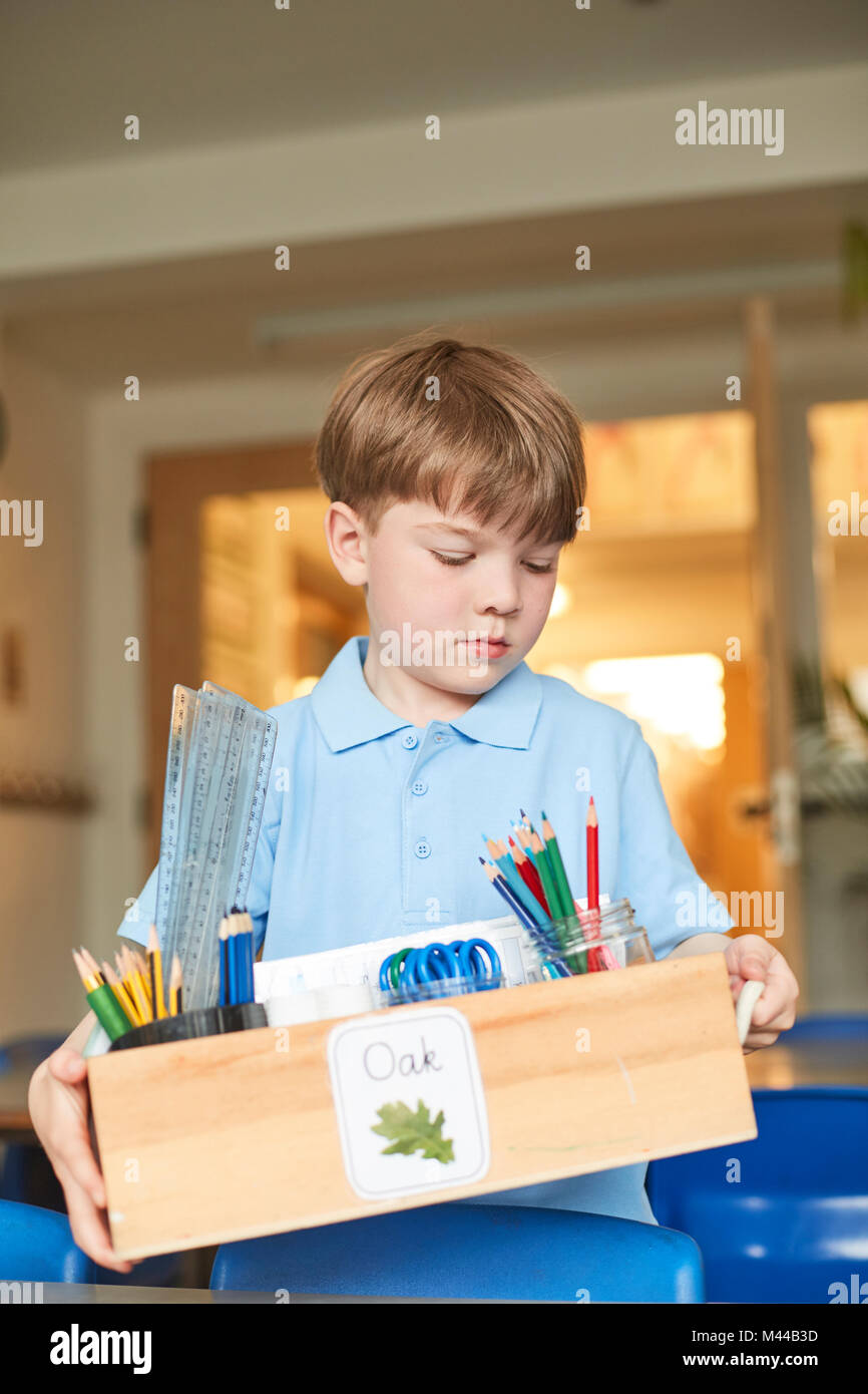 Schoolboy carrying box of pencils in classroom at primary school Stock Photo