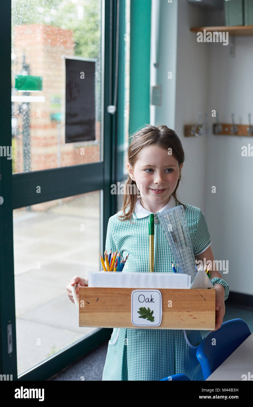 Schoolgirl carrying box of pencils in classroom at primary school Stock Photo