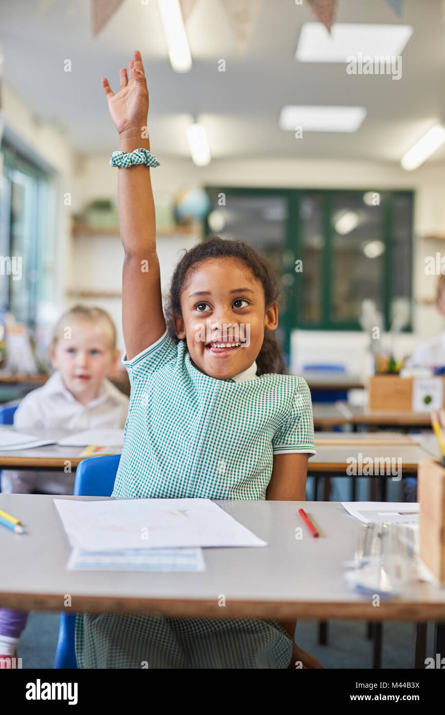 Schoolgirl with hand up in classroom at primary school Stock Photo