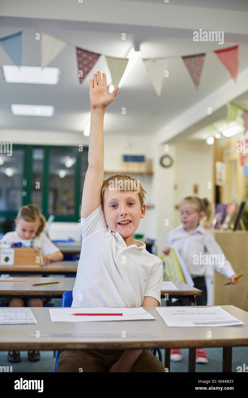 Schoolboy with hand up in classroom at primary school Stock Photo