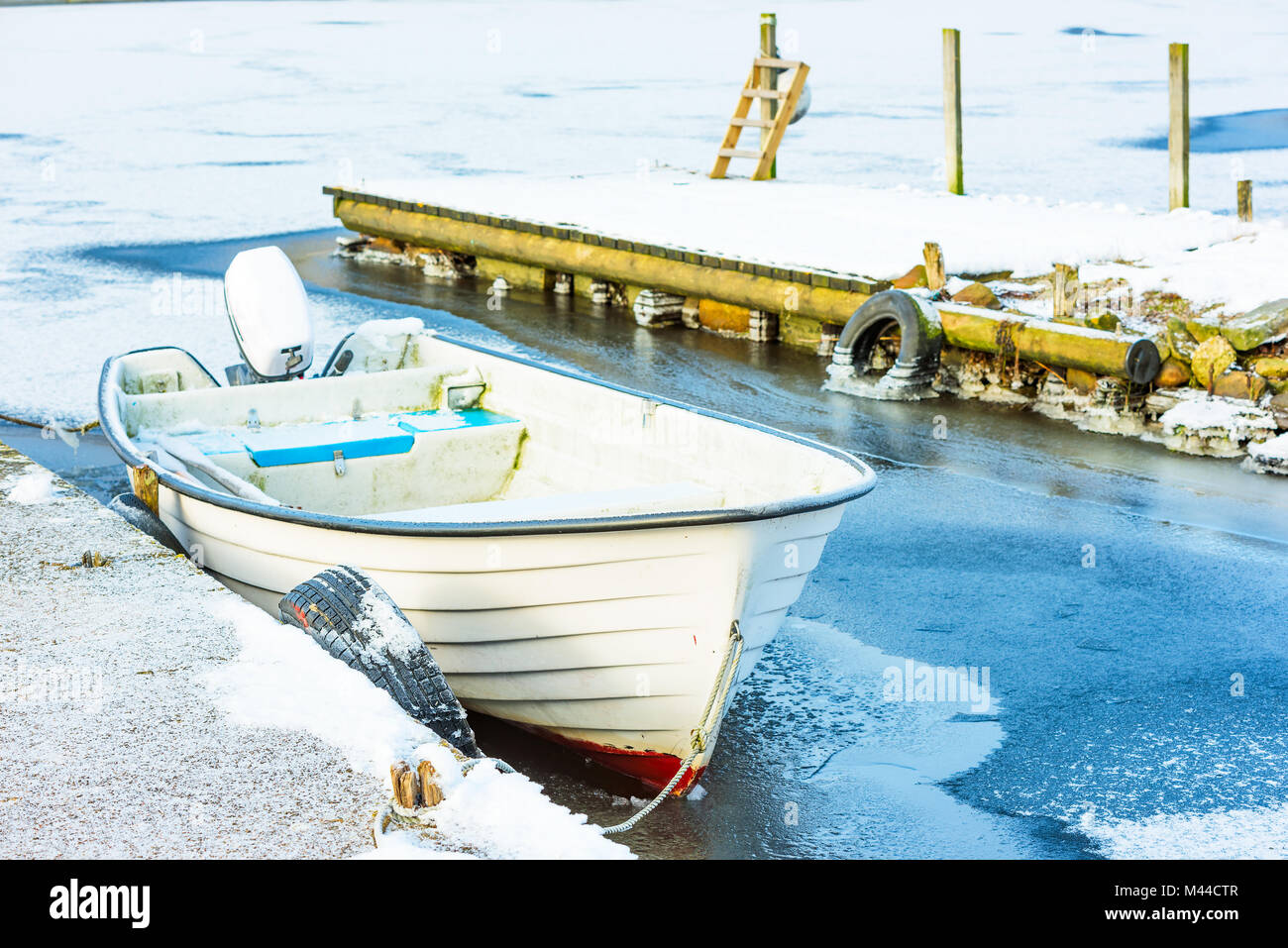 Open white motorboat stuck in ice by a pier. Stock Photo
