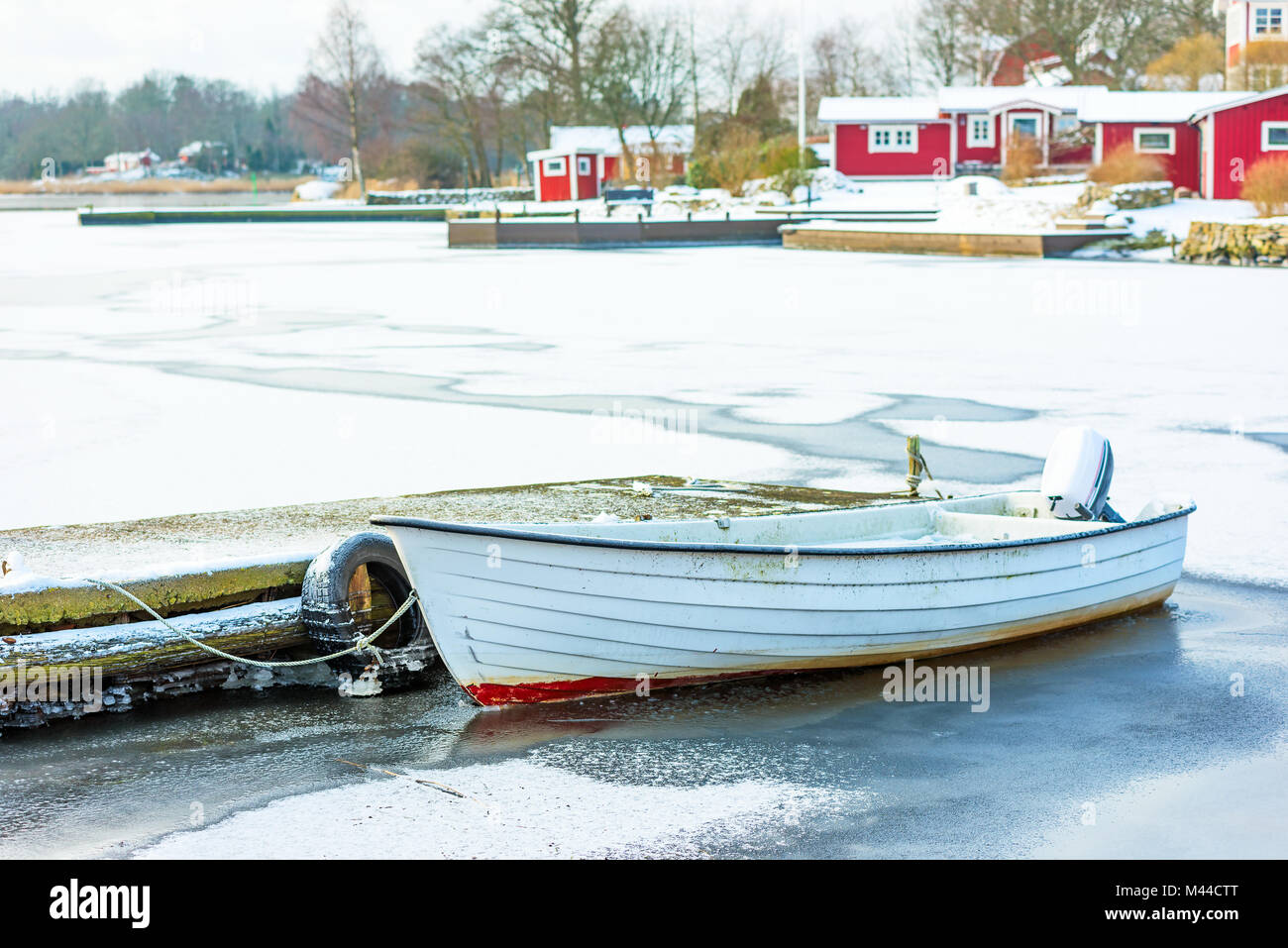 Open white motorboat stuck in ice by a pier in a fishing village. Stock Photo