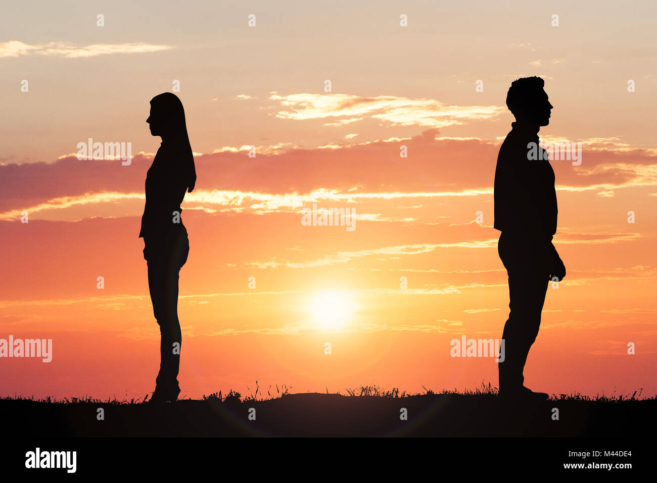 Couple Silhouette Standing Away From Each Other Against Dramatic Sky At Sunset Stock Photo