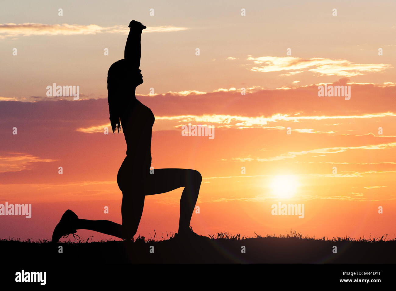 Silhouette Of A Woman Stretching Against Dramatic Sky At Sunset Stock Photo