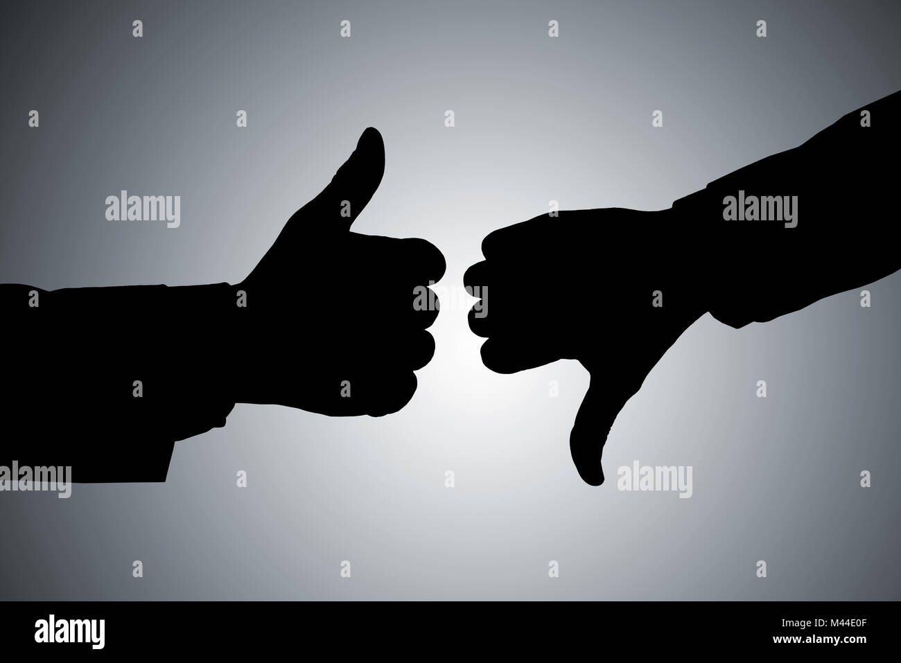 Silhouette Of Two Person's Hand Showing Thumb Up And Thumb Down Against Gray Background Stock Photo