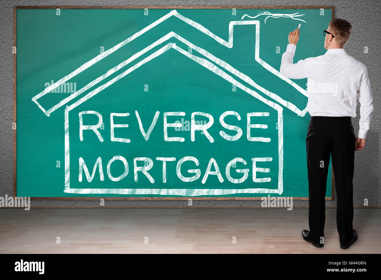 Full length rear view of businessman drawing house with reverse mortgage text on blackboard Stock Photo
