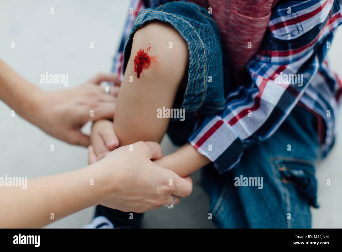 Mothers hands holding a little injured boy with a scraped knee Stock Photo