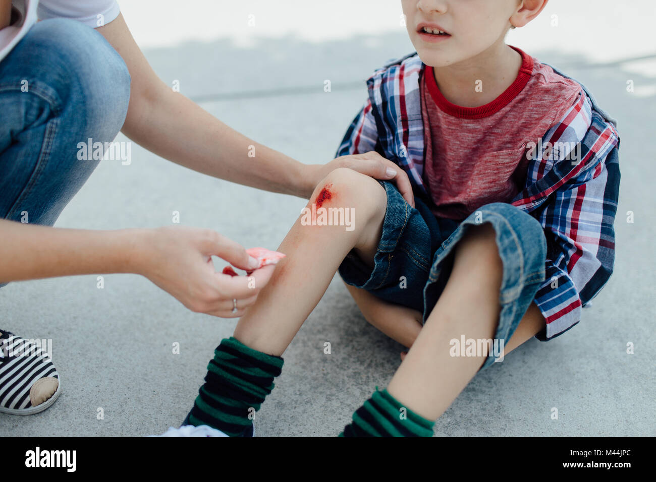 Mother nurses a bleeding knee of her son after an accident in a playground Stock Photo