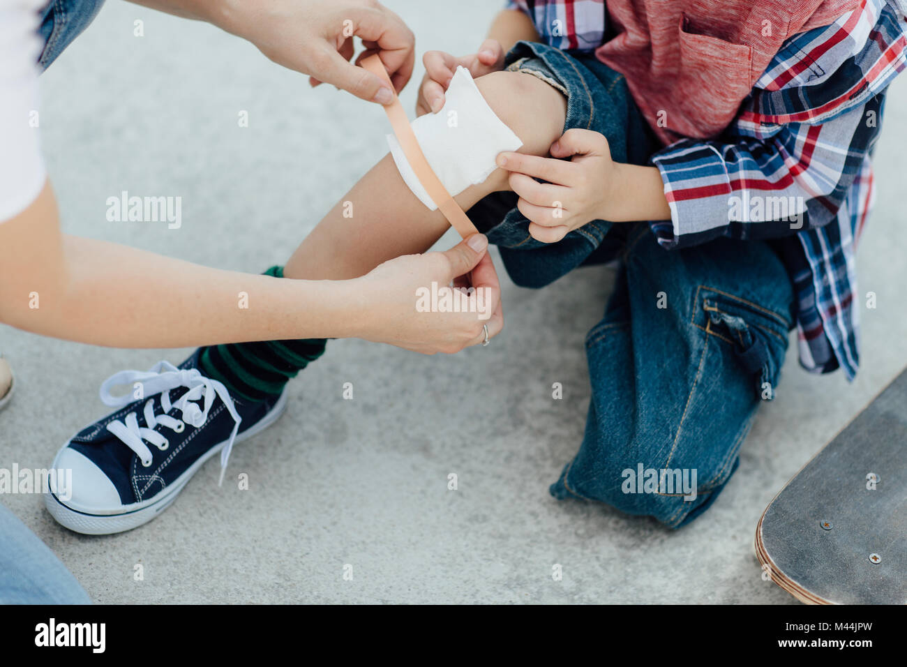 Mother nurses a bleeding cut of her skateboarding son and puts a plaster on his knee Stock Photo