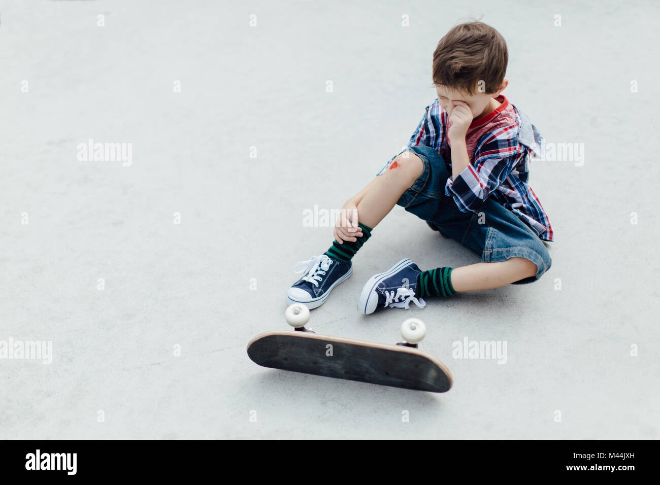 Portrait of an upset young skater boy sitting on a floor in pain Stock Photo