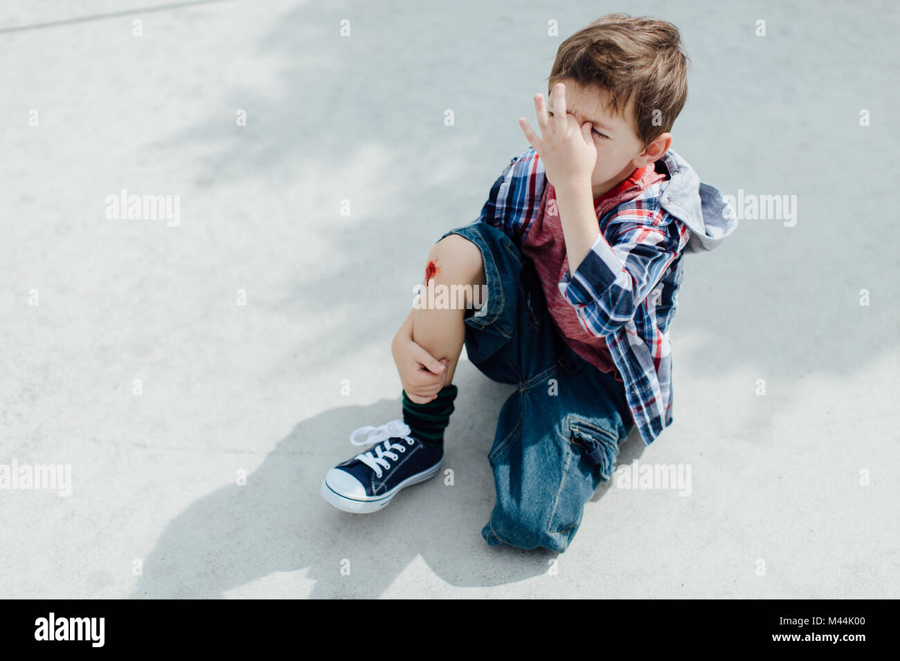 Injured little boy sitting on concrete floor with a scraped knee Stock Photo
