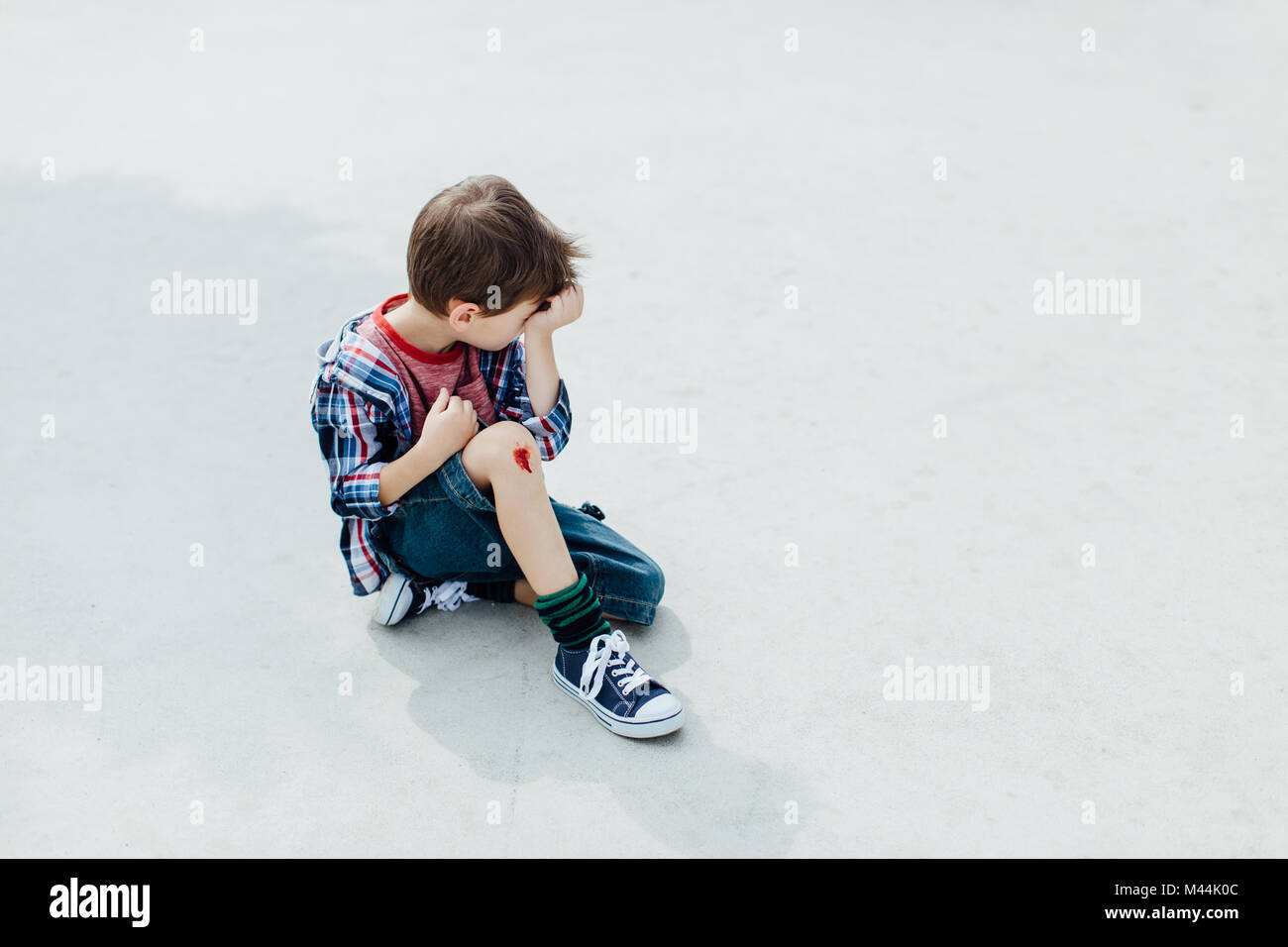 Injured little boy sitting on concrete floor with a bleeding knee Stock Photo