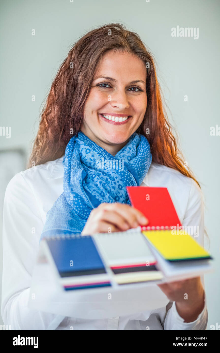 Portrait of smiling young female fashion designer choosing red color from swatches in office Stock Photo