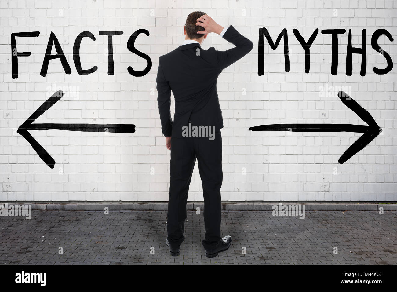 Rear view of confused businessman looking at arrow signs below facts and myths text Stock Photo