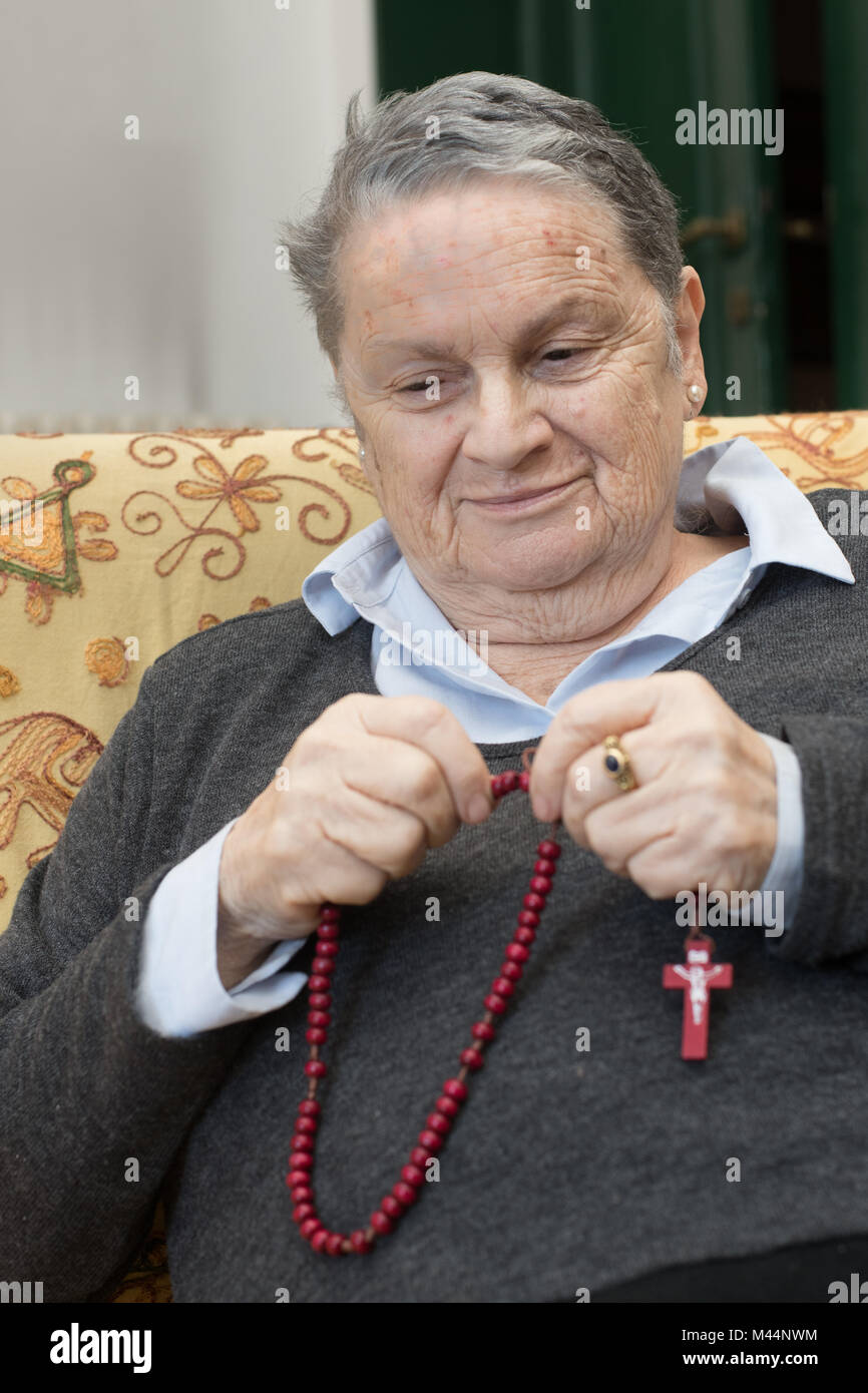 Elderly woman portrait praying say the rosary and smiling, christianity religion lifestyle Stock Photo