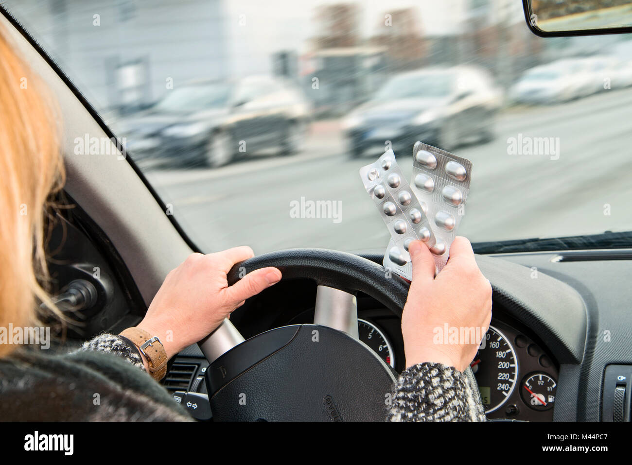 Hands with packs of tablets at the steering wheel of a car while driving Stock Photo