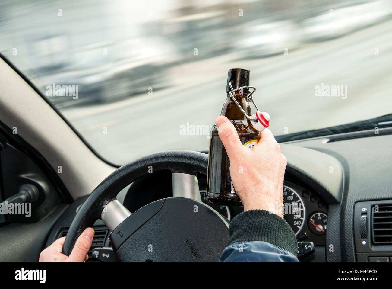 Opened bottle of beer and hands on the steering wheel of a car Stock Photo