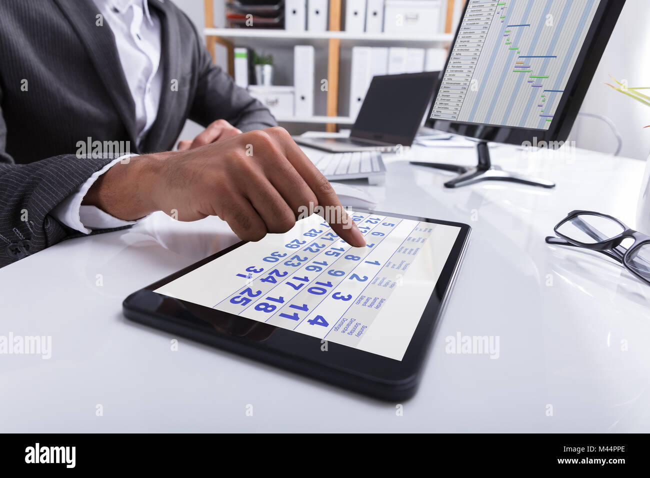 Close-up Of A Businessperson's Hand Using Calendar On Digital Tablet At Workplace Stock Photo