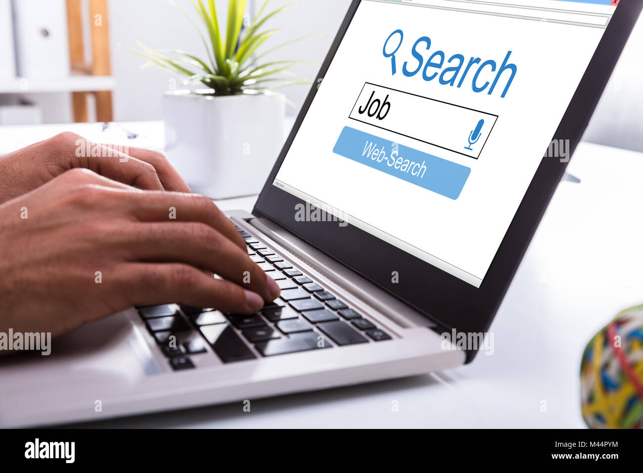 Close-up Of A Businessperson's Hand Searching Online Job On Laptop At Workplace Stock Photo