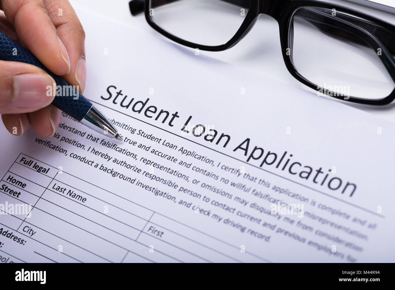 Close-up Of A Person's Hand Filling Student Loan Application Form Stock Photo