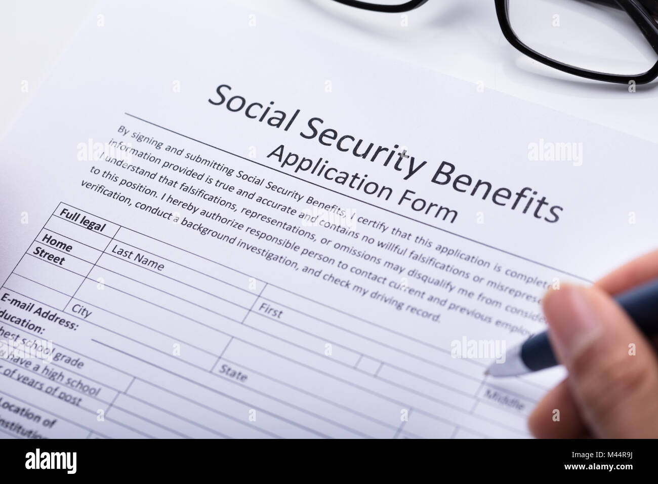 Close-up Of A Person's Hand Filling Social Security Benefits Application Form Stock Photo