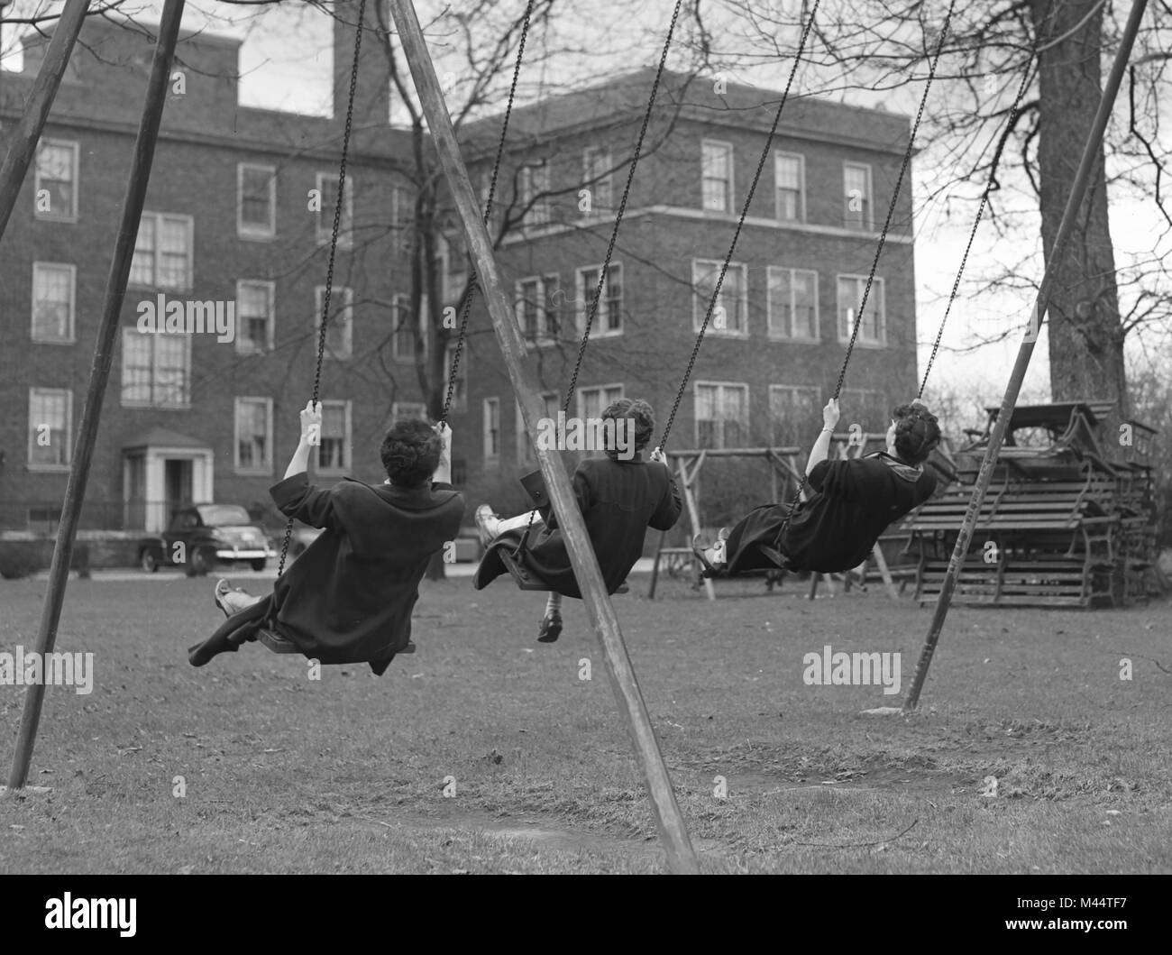 Rear view of three adult women playing on a swing set in Chicago, ca. 1950. Stock Photo