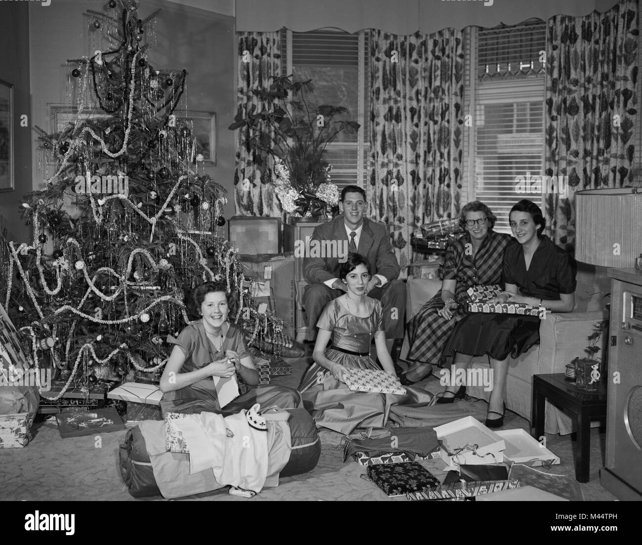 American family gathers around the tree to open presents on Christmas morning, ca. 1960. File name: Stock Photo