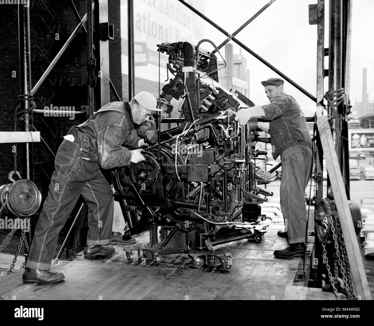 Three workers moving part of a printing press on a loaded dock in the late 1958. Stock Photo
