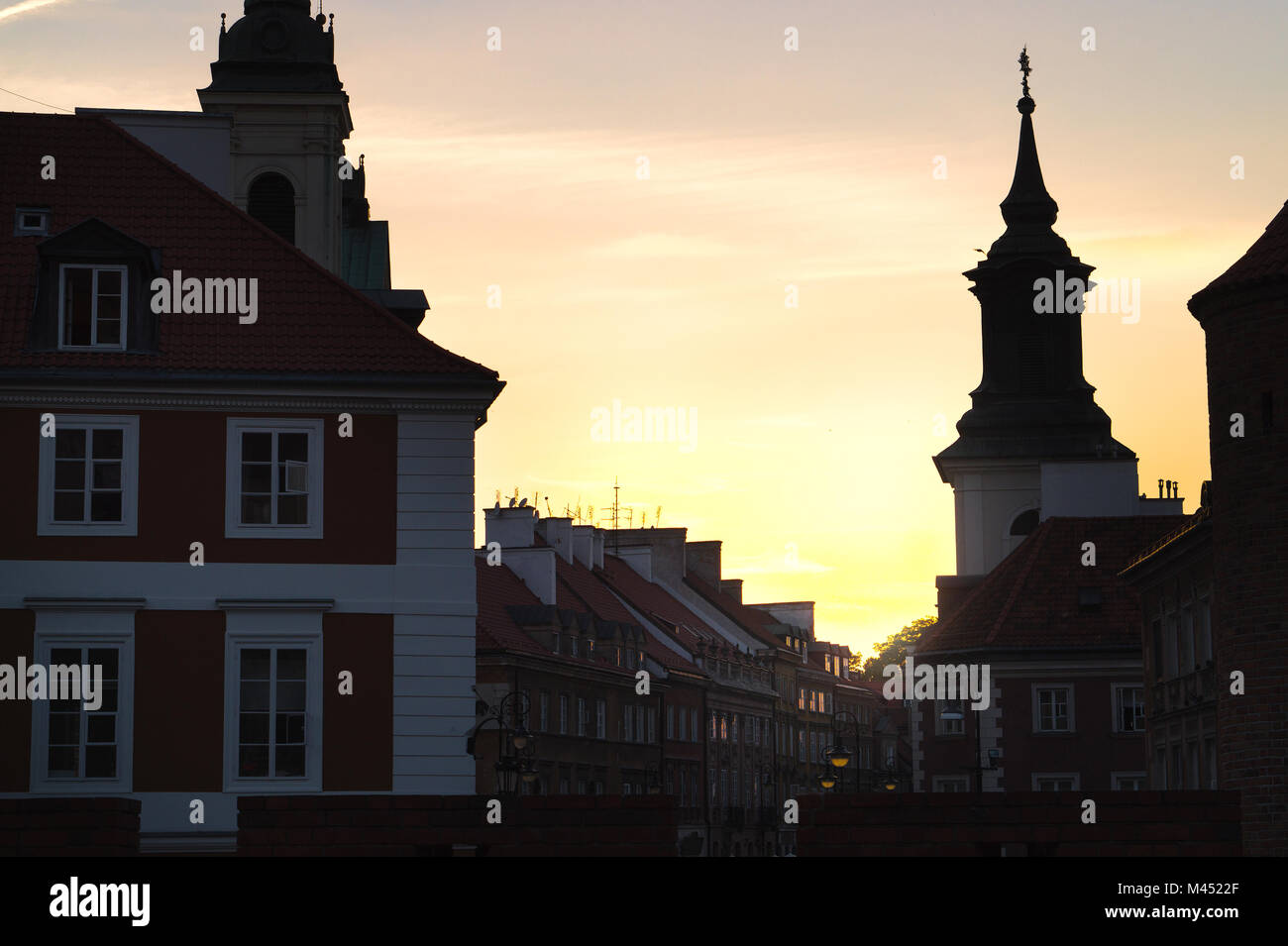 Sunset or sunrise in old town of Warsaw, Poland. Old buildings in dark shadow, almost silhouette. Beautiful yellow orange sky. Stock Photo