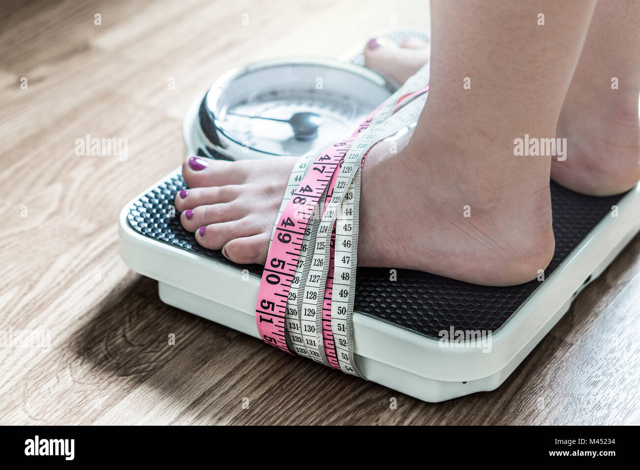 Feet tied up with measuring tape to a weight scale. Addiction and obsession to weight loss. Anorexia and eating disorder concept. Stock Photo