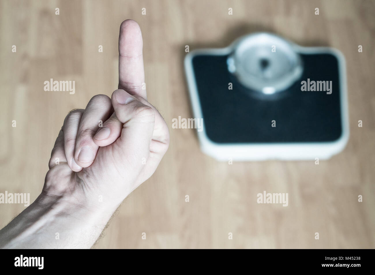 Hand showing middle finger to weight scale. Flipping the bird. Man frustrated and angry from being overweight and obese. Problem and failure in weight Stock Photo