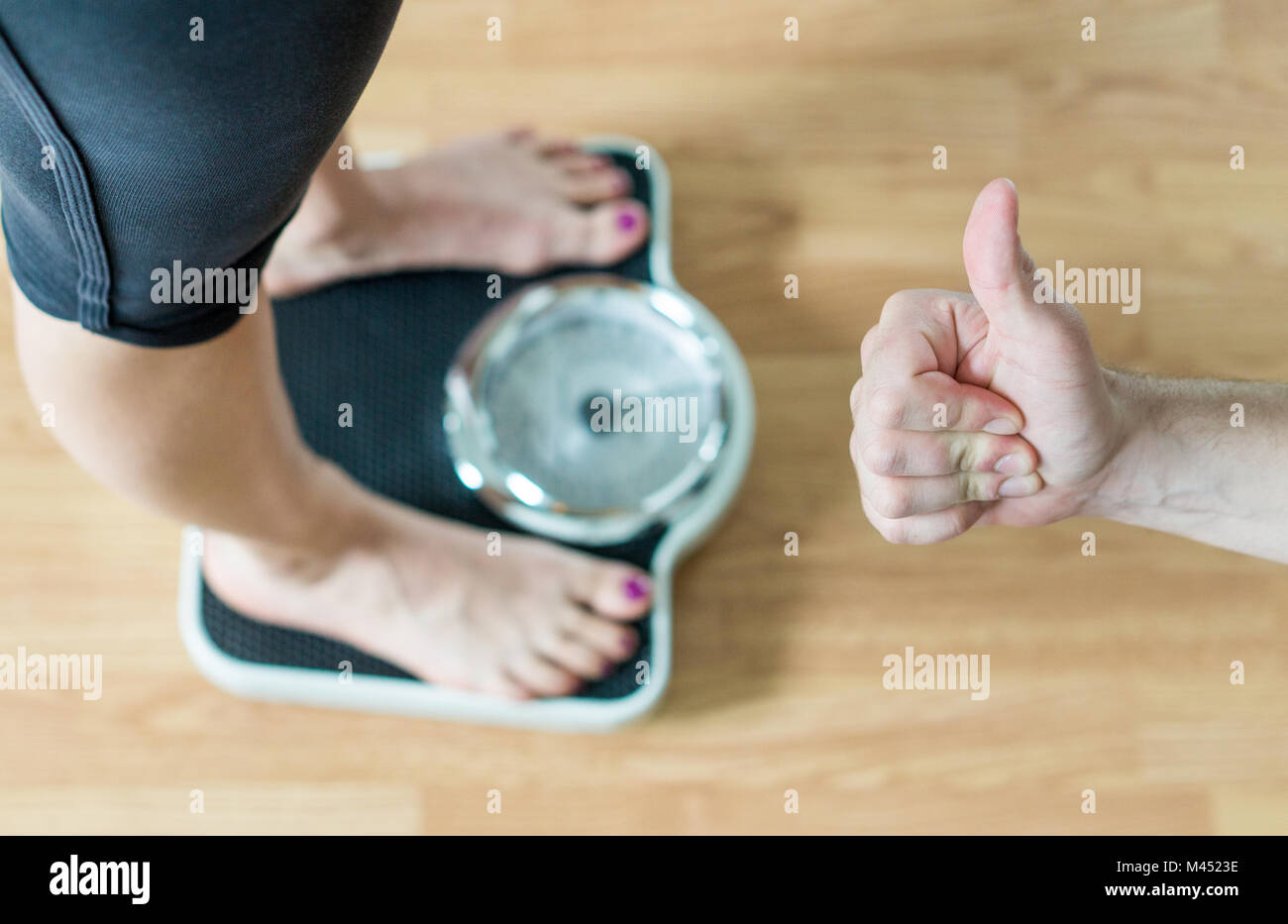 Personal trainer or coach giving thumbs up to a person standing on scale. Success and great achievement in weight loss. Encouragement and motivation.  Stock Photo