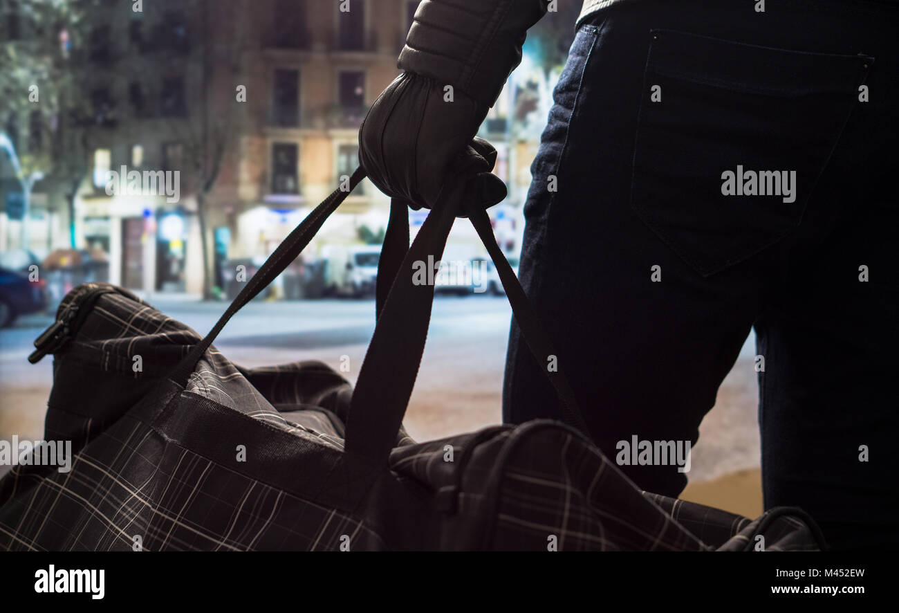 Terrorist standing and holding black bomb bag in hand with leather gloves. Man planning a dangerous explosion in city center. Suicide bomber at night. Stock Photo