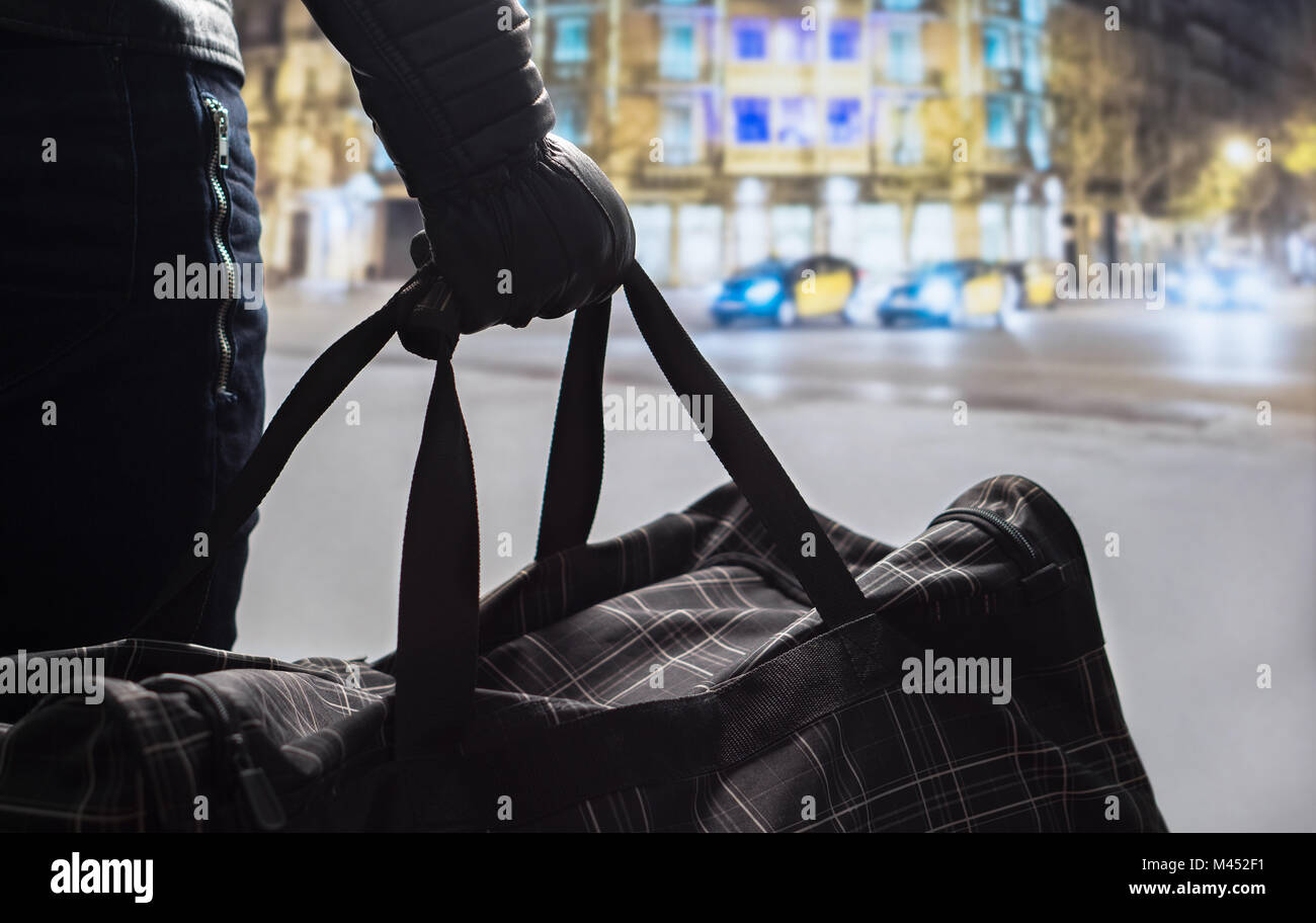 Terrorism and security threat concept. Terrorist at night. Suspicious man standing in city center holding black bag. Planning a bomb attack. Stock Photo