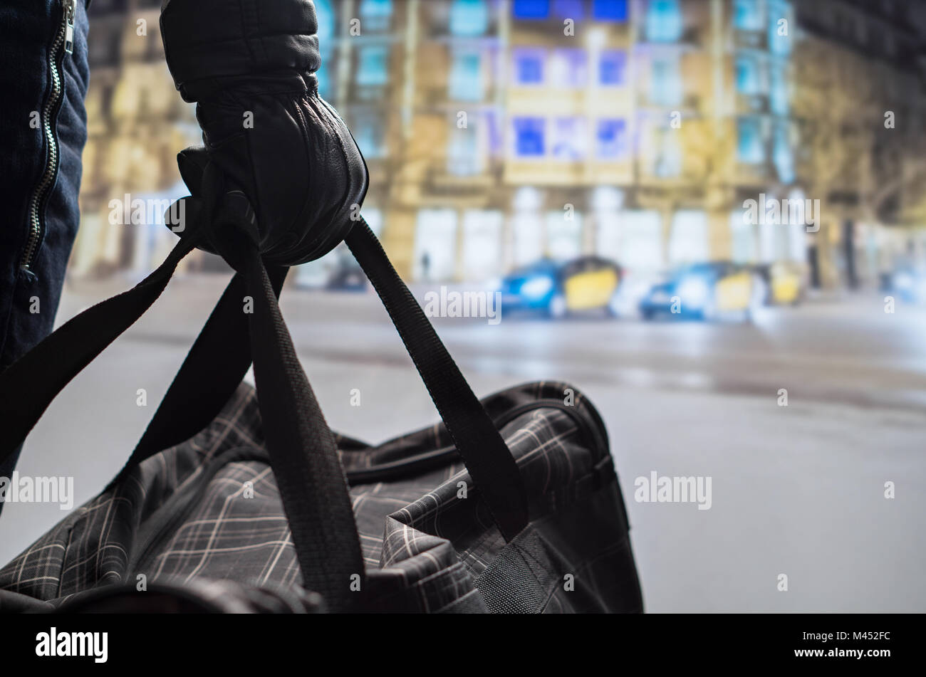 Close up of terrorist holding black bomb bag in hand. Suicide bomber planning dangerous explosion in city center at night. Traffic, cars and buildings Stock Photo