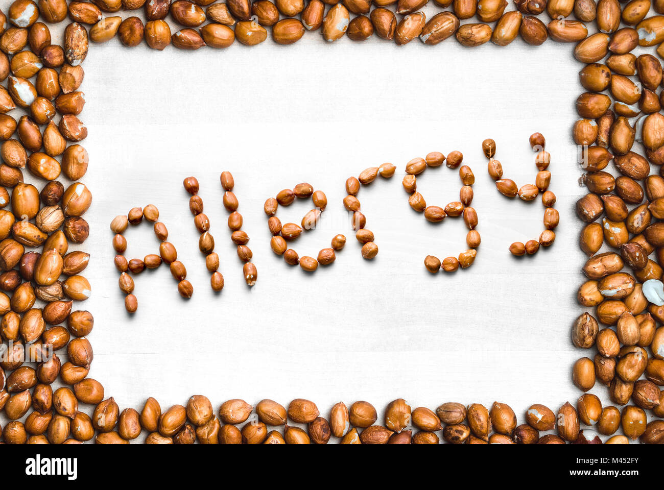 Allergy written with peanuts and surrounded with nut frame. Word and text made from nuts. Groundnuts on white wooden table or board with border. Stock Photo