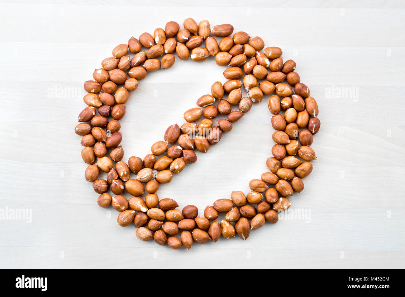 Peanut allergy. Stop, forbidden, prohibited and banned sign and symbol formed with nuts on white wooden table or board. No groundnuts for allergen. Stock Photo