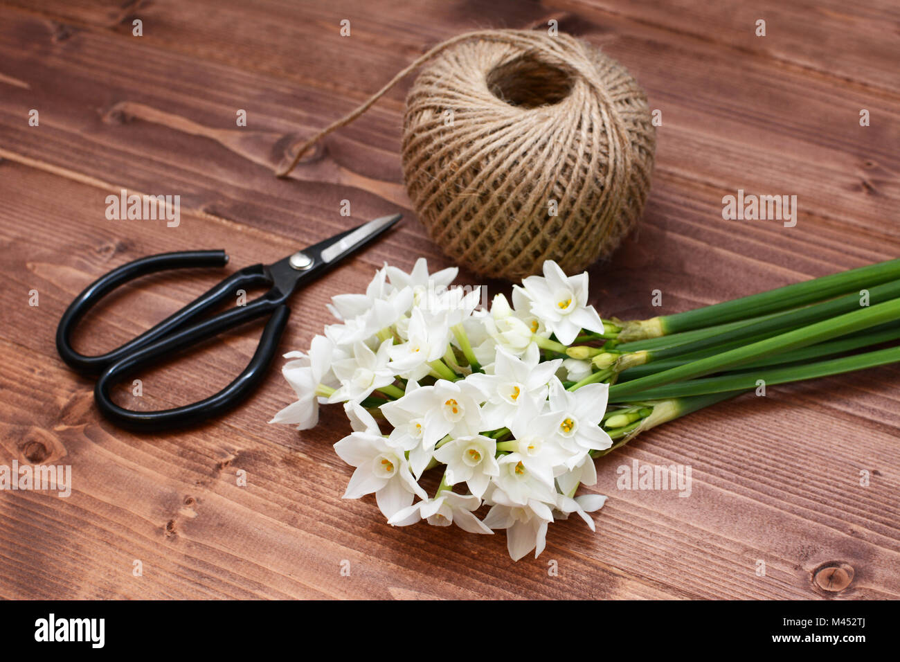 Old-fashioned florist scissors with a bunch of white narcissi and a ball of twine, gathered on a wooden table Stock Photo