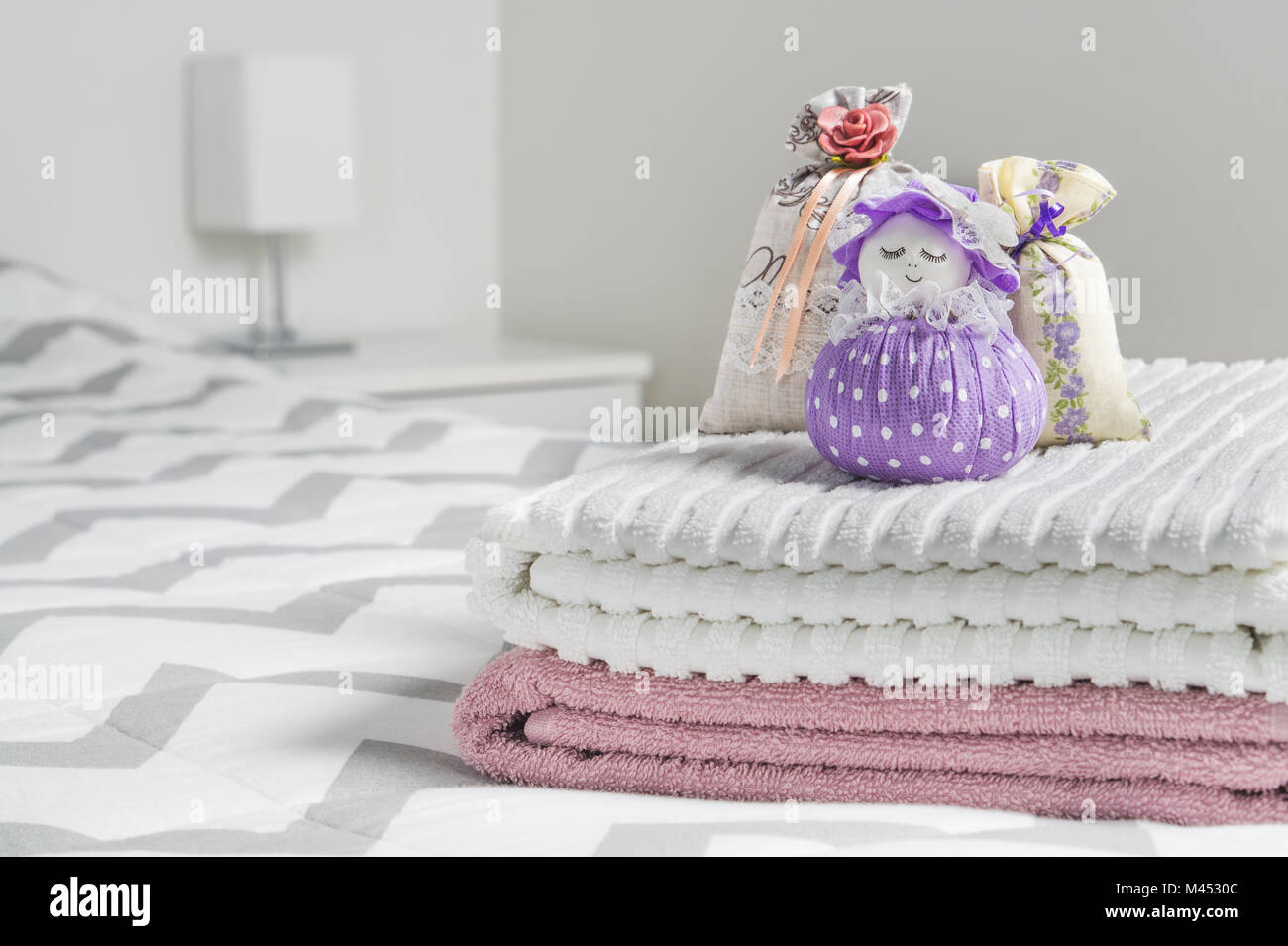 Scented sachets and fragrant pouch figure of a girl. Bags filled with lavender in bedroom. Towels on bed. Decoration accessories and light color. Stock Photo